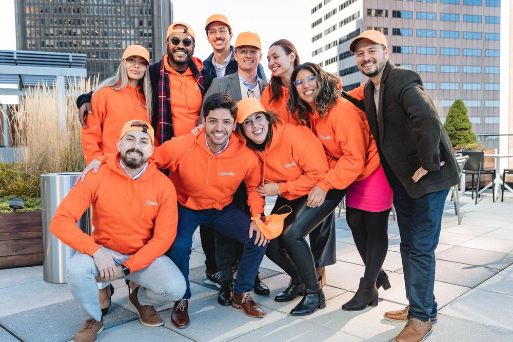 Team wearing coordinated orange hoodies posing together on urban rooftop.