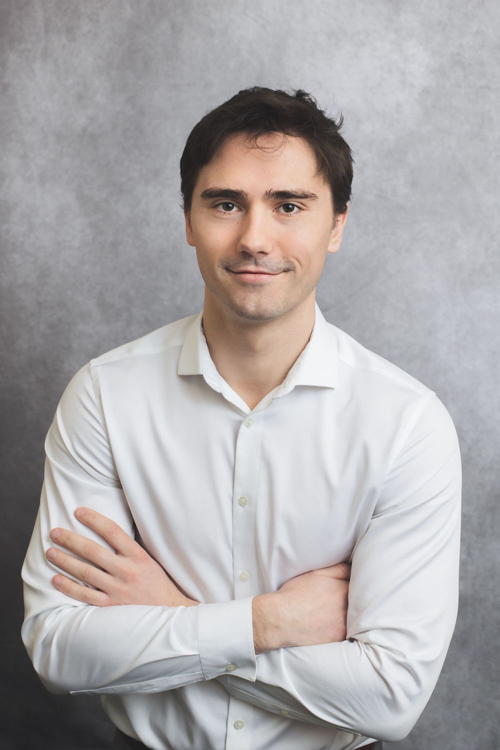 Professional portrait against grey background wearing crisp white button-down shirt.