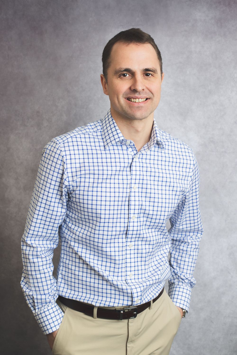 Professional headshot of person in checkered button-down shirt against grey background.