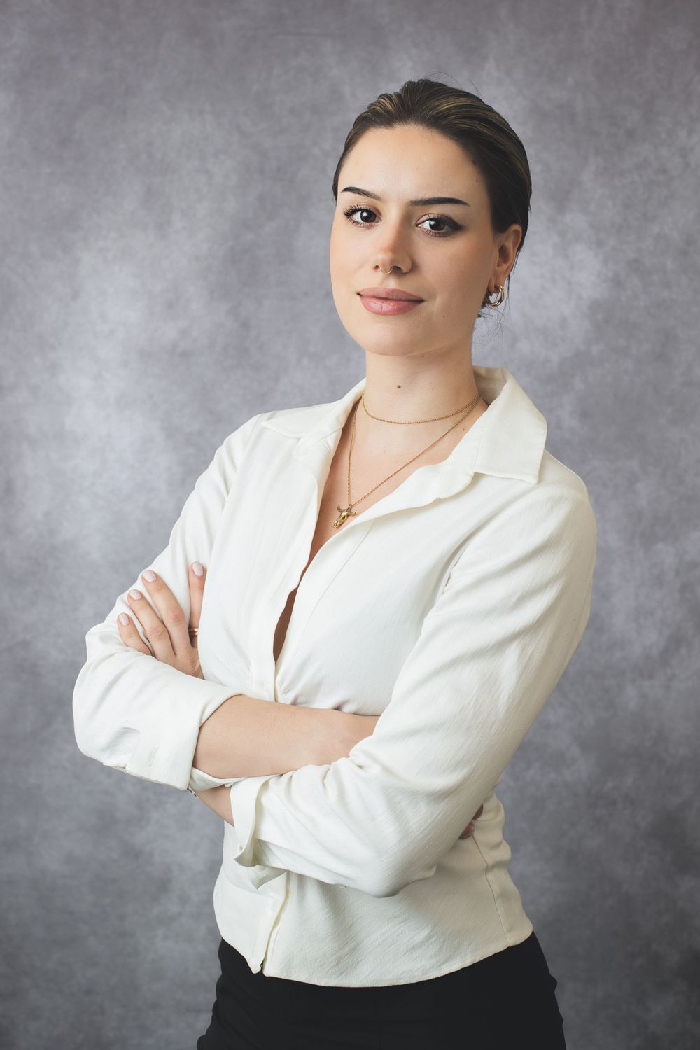 Professional portrait of person in white blouse with jewelry against grey background.