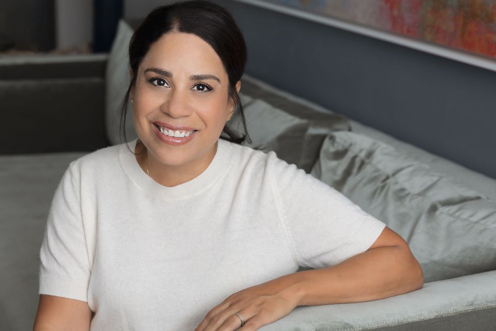 Professional headshot of someone in a white t-shirt against a modern interior background.