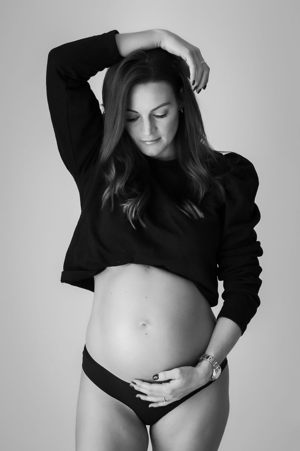 Black and white image of pregnant woman with one hand on belly and one hand over head