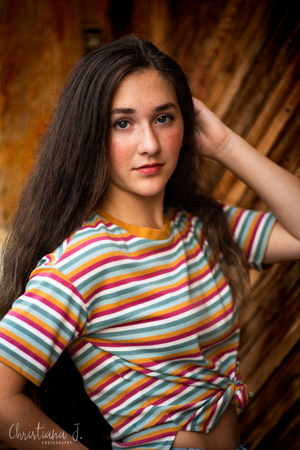 Portrait in colorful striped shirt against wooden backdrop.