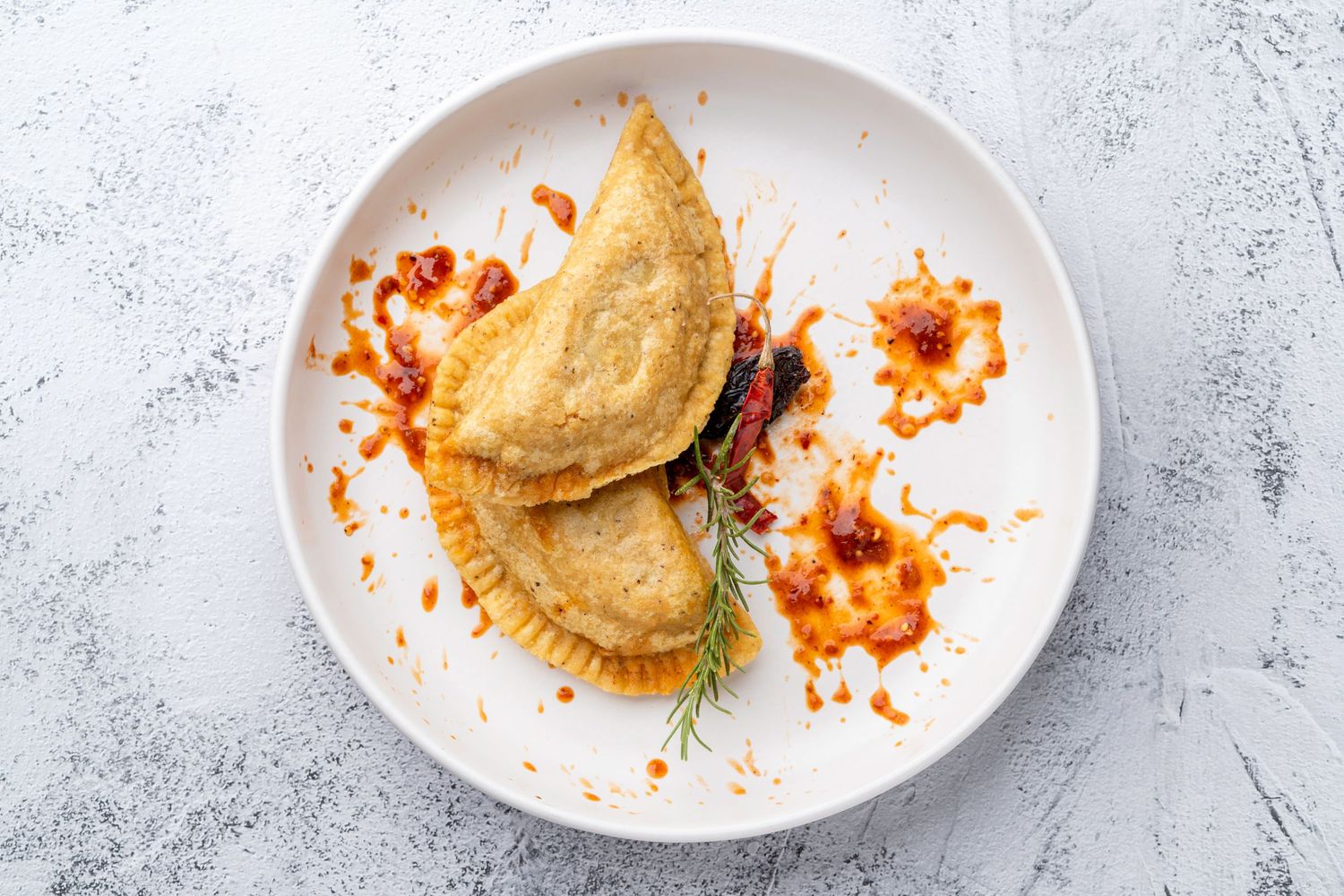 Partially eaten empanadas or pastries with orange sauce drizzled on white plates.