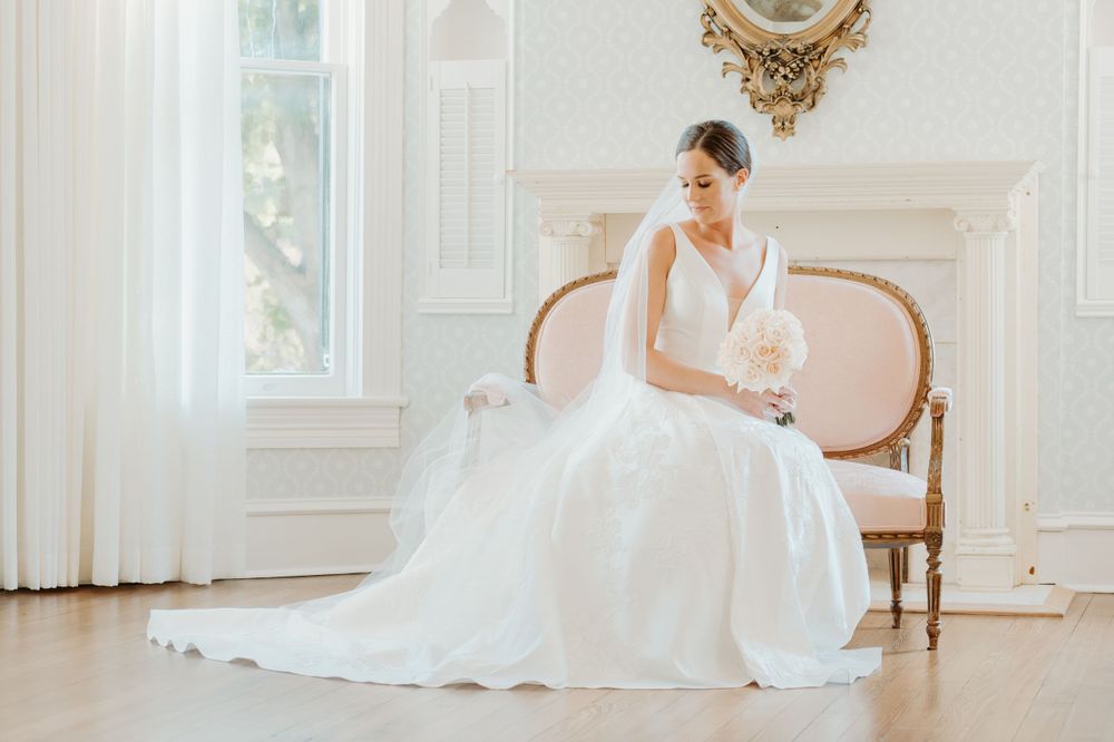 Classic bridal portrait in white gown seated in elegant room with ornate gold mirror.