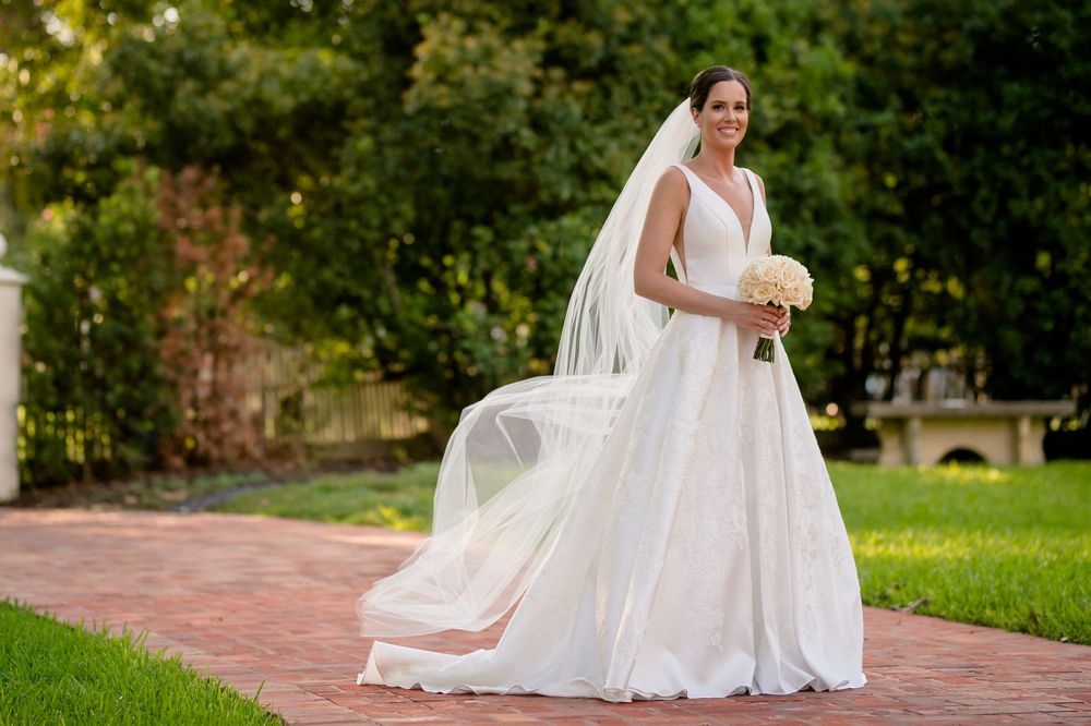 Elegant bridal portrait outdoors with flowing veil catching breeze on brick pathway.