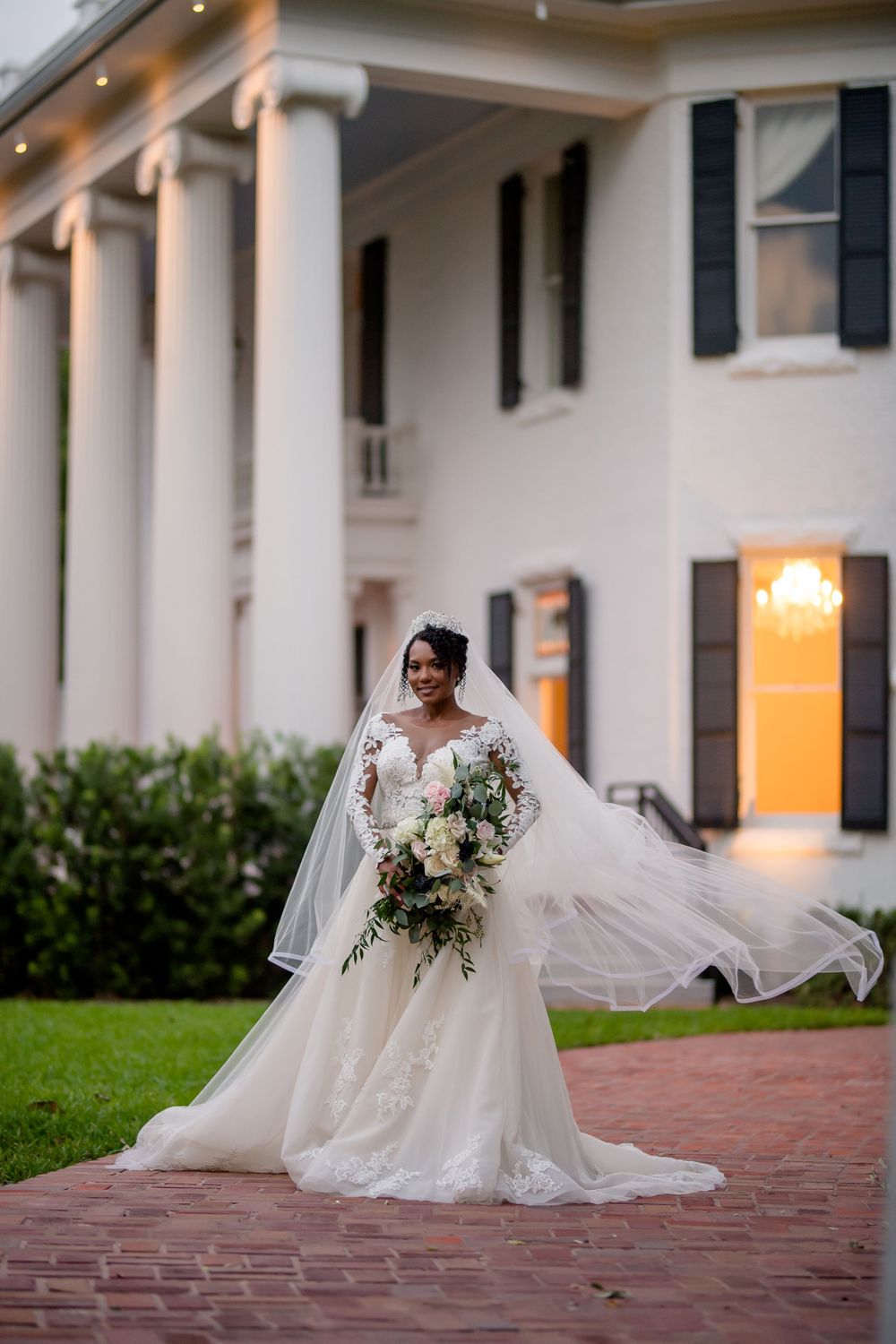 Dramatic evening bridal portrait with flowing veil outside historic columned mansion.