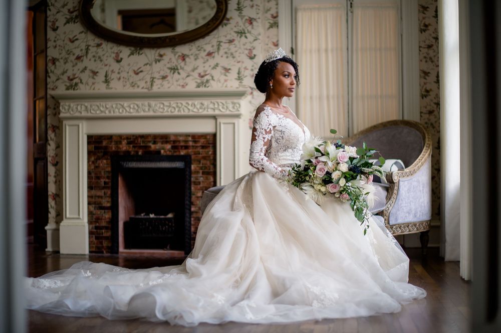 Romantic bridal portrait in lace gown by vintage fireplace with floral bouquet.