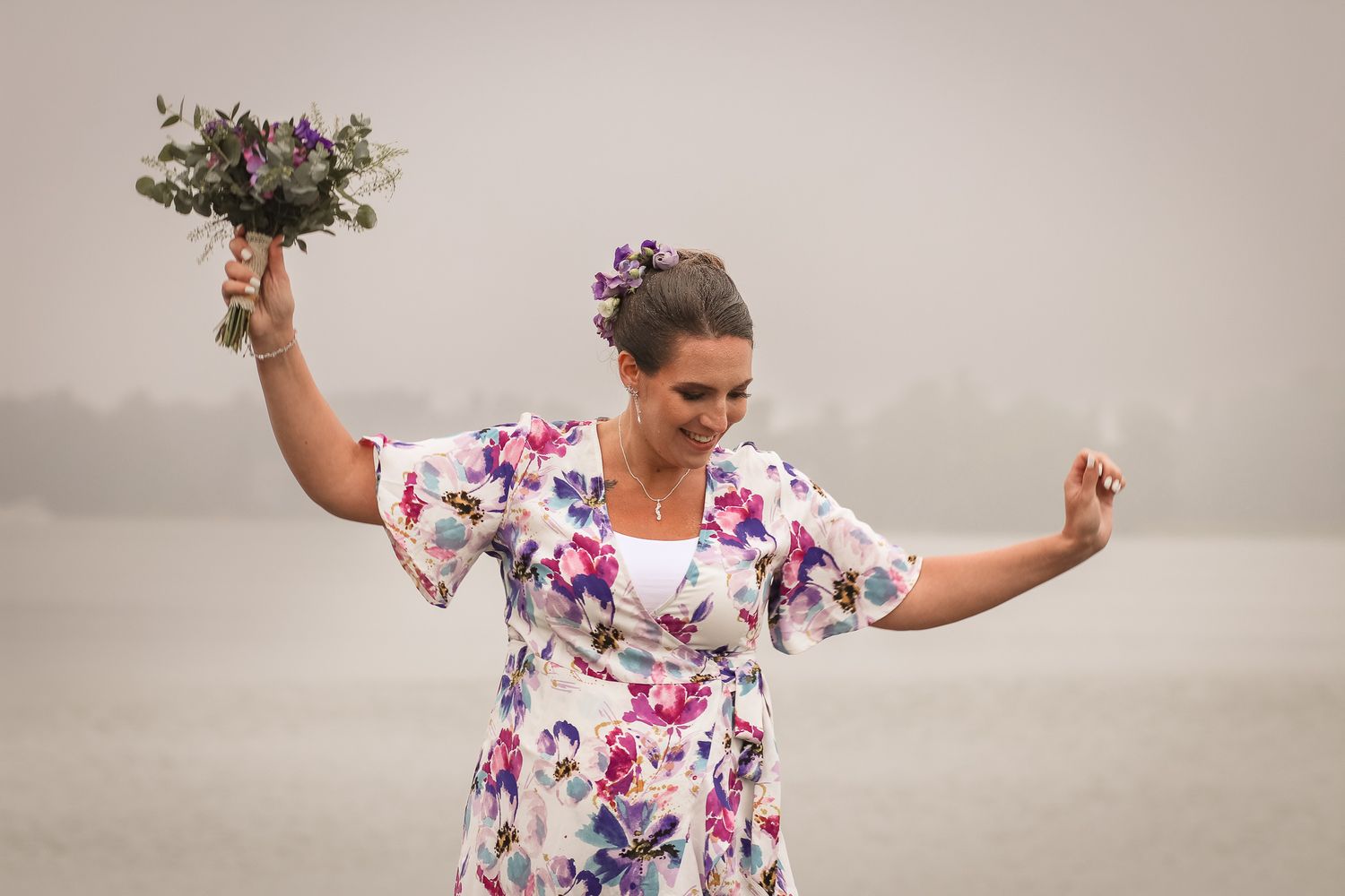 Pregnant woman with flower bouqet and white flower dress, dancing in the rain. Foggy background.