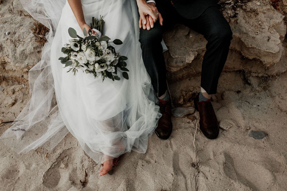 bride and groom sitting on a log with bouquet and details