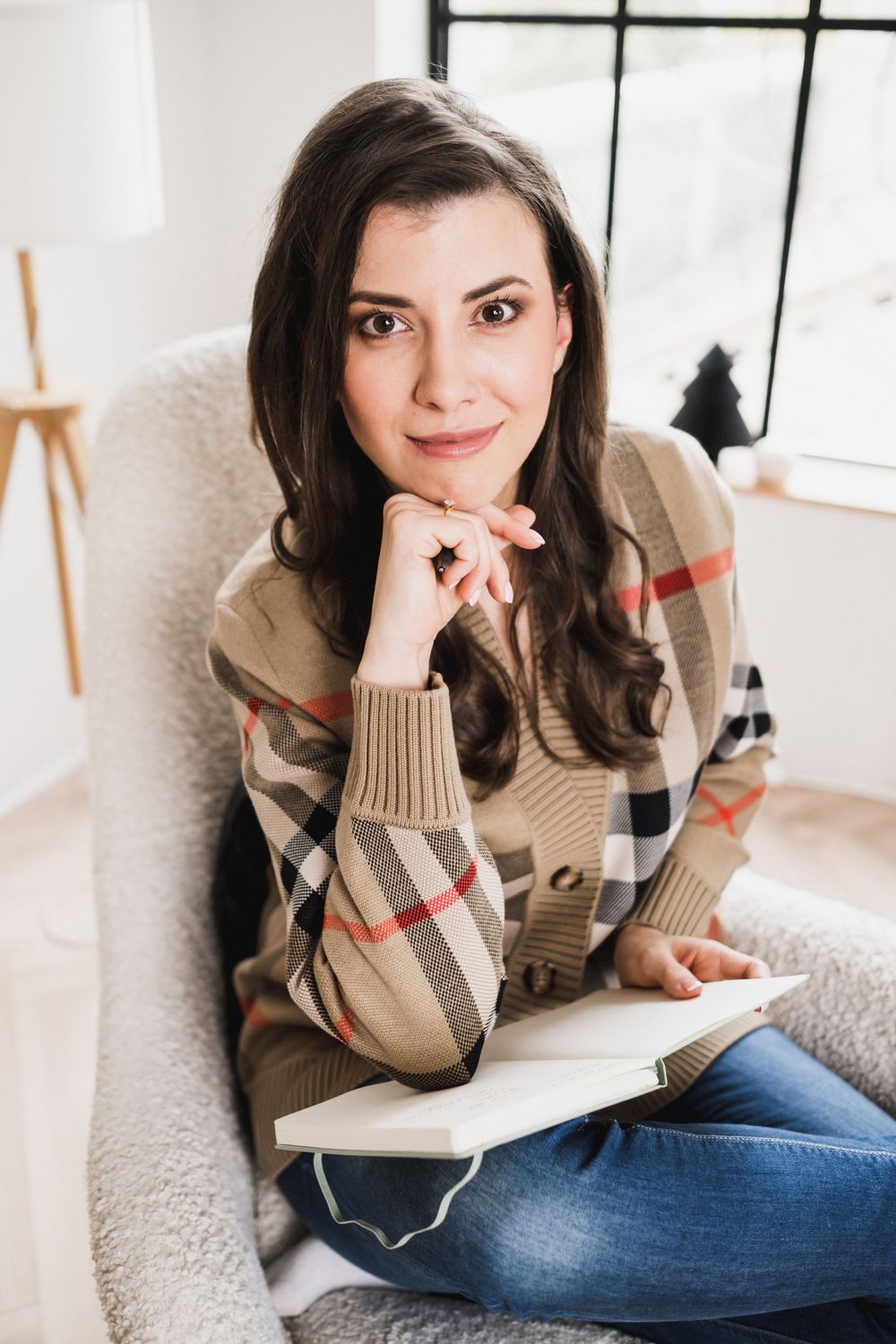 Woman in plaid cardigan relaxing in armchair while writing.