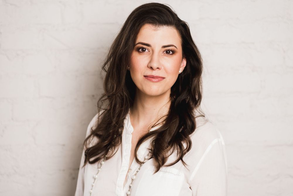 Professional headshot of woman with dark hair wearing white blouse against light background.