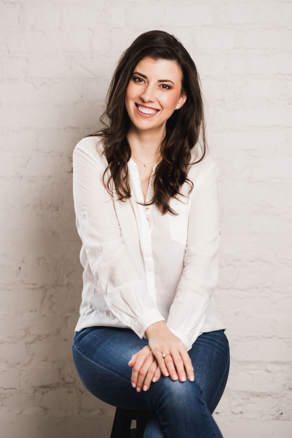 Woman in white button-down shirt smiling at camera against light wall.