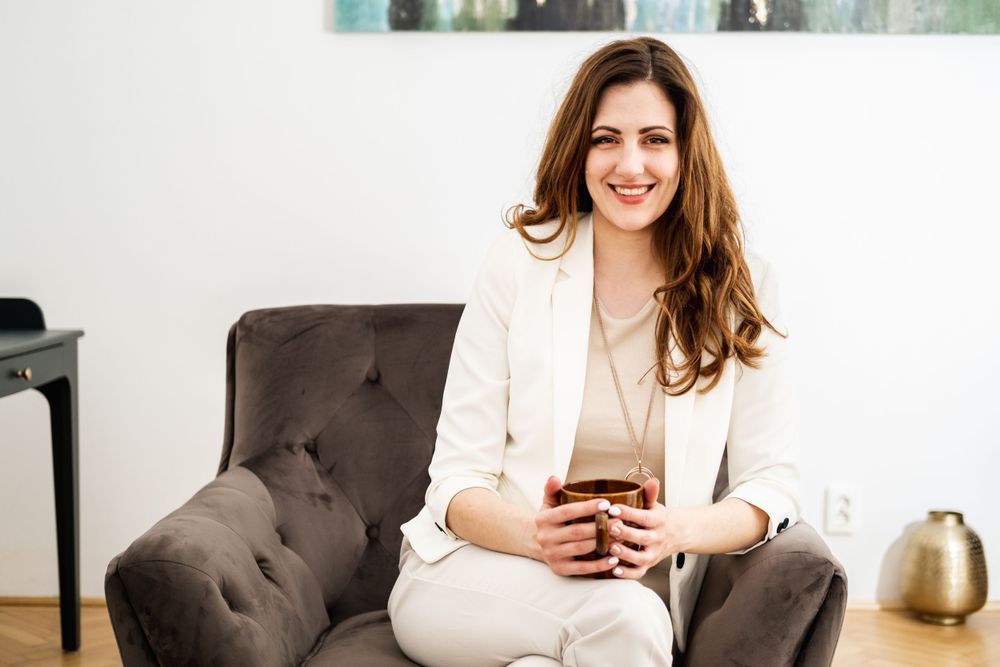 Businesswoman in white suit holding phone while sitting in armchair.
