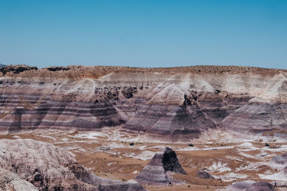 Colorful layered badlands rock formations under a clear blue sky in Petrified Forest National Park.