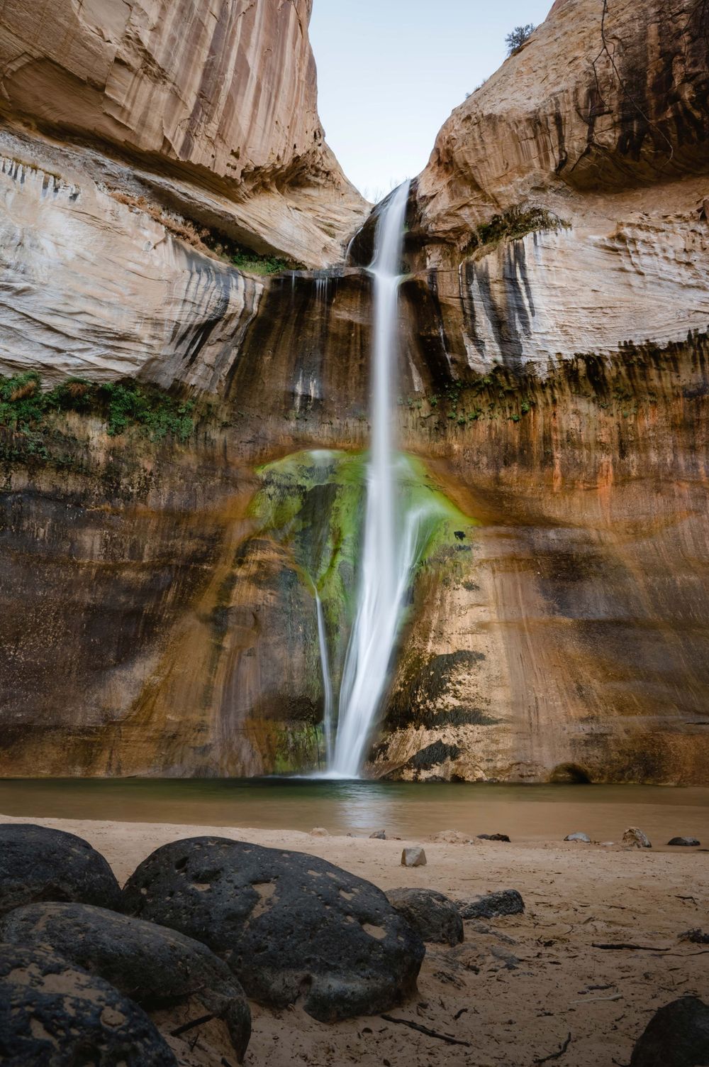 Majestic waterfall cascades down smooth sandstone canyon walls into a tranquil pool at Calf Creek Falls, Utah.