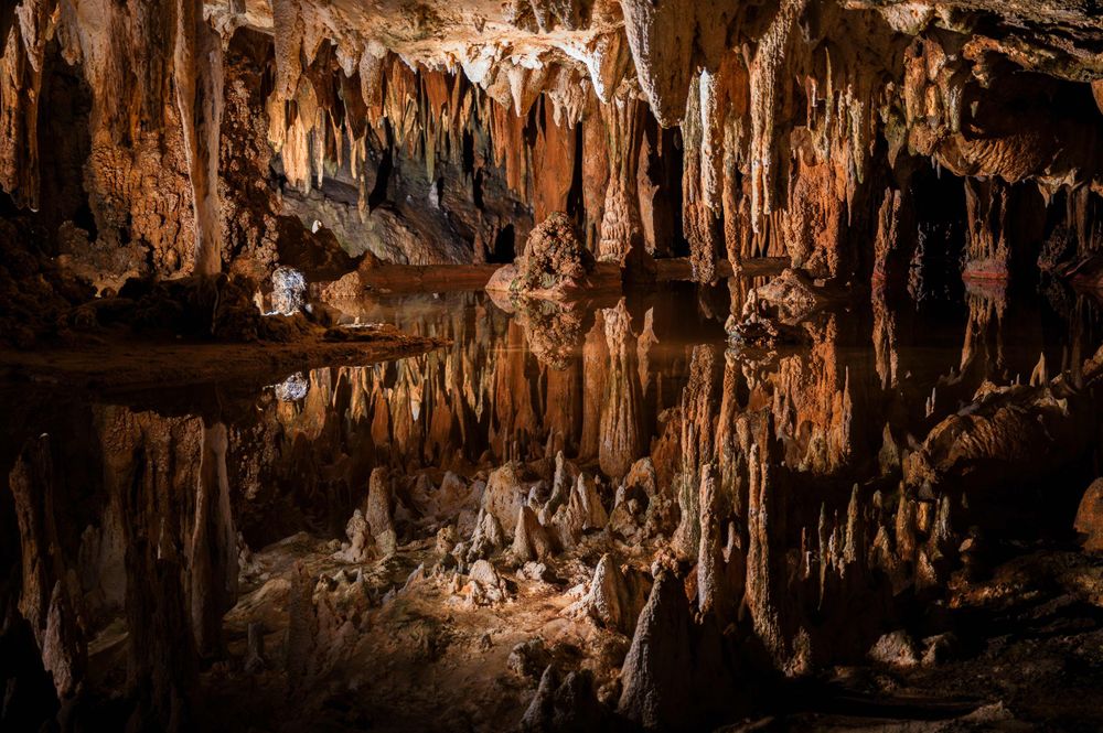 Stunning cave interior with stalactites and stalagmites reflected in a still underground pool.
