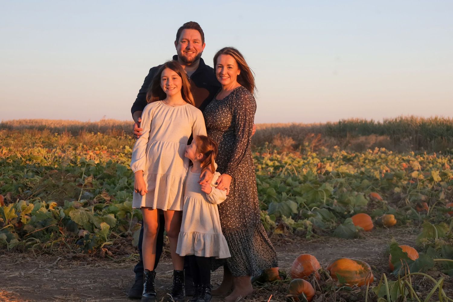 Family photo session in pumpkin patch field during golden hour sunset.