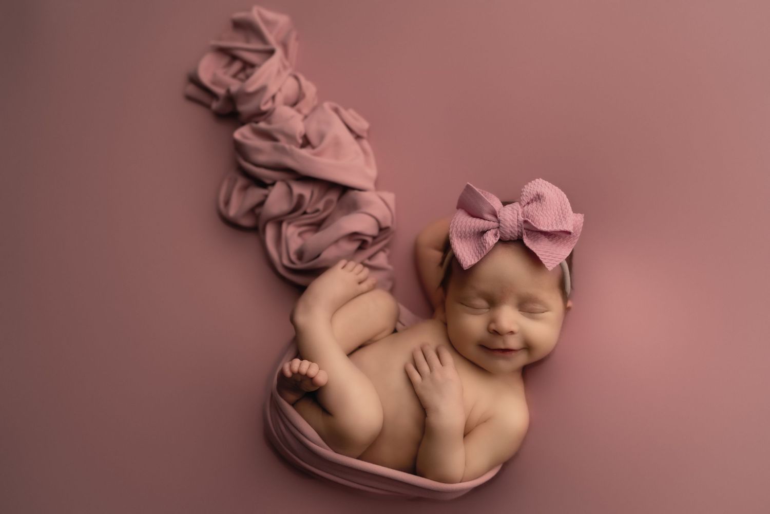 Sleeping newborn posed with pink accessories on matching pink backdrop.
