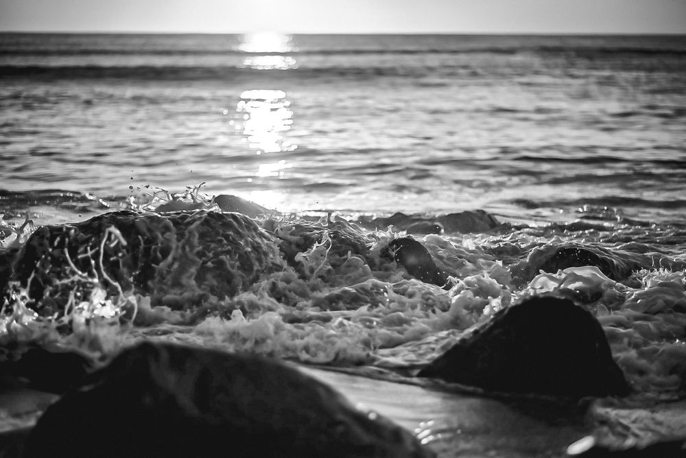 Black and white seascape showing waves and sunlight reflection on ocean surface.