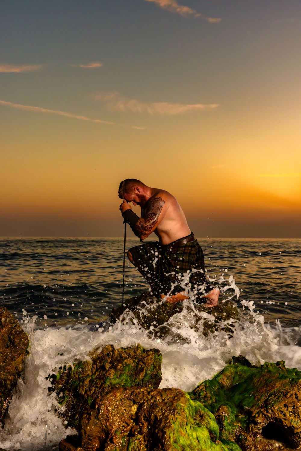Waves crash dramatically against mossy rocks during golden hour at the beach.