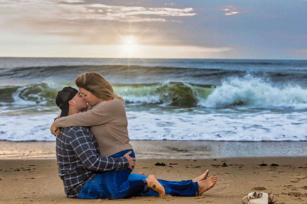 Couple embracing on sandy beach at sunset with ocean waves in background.