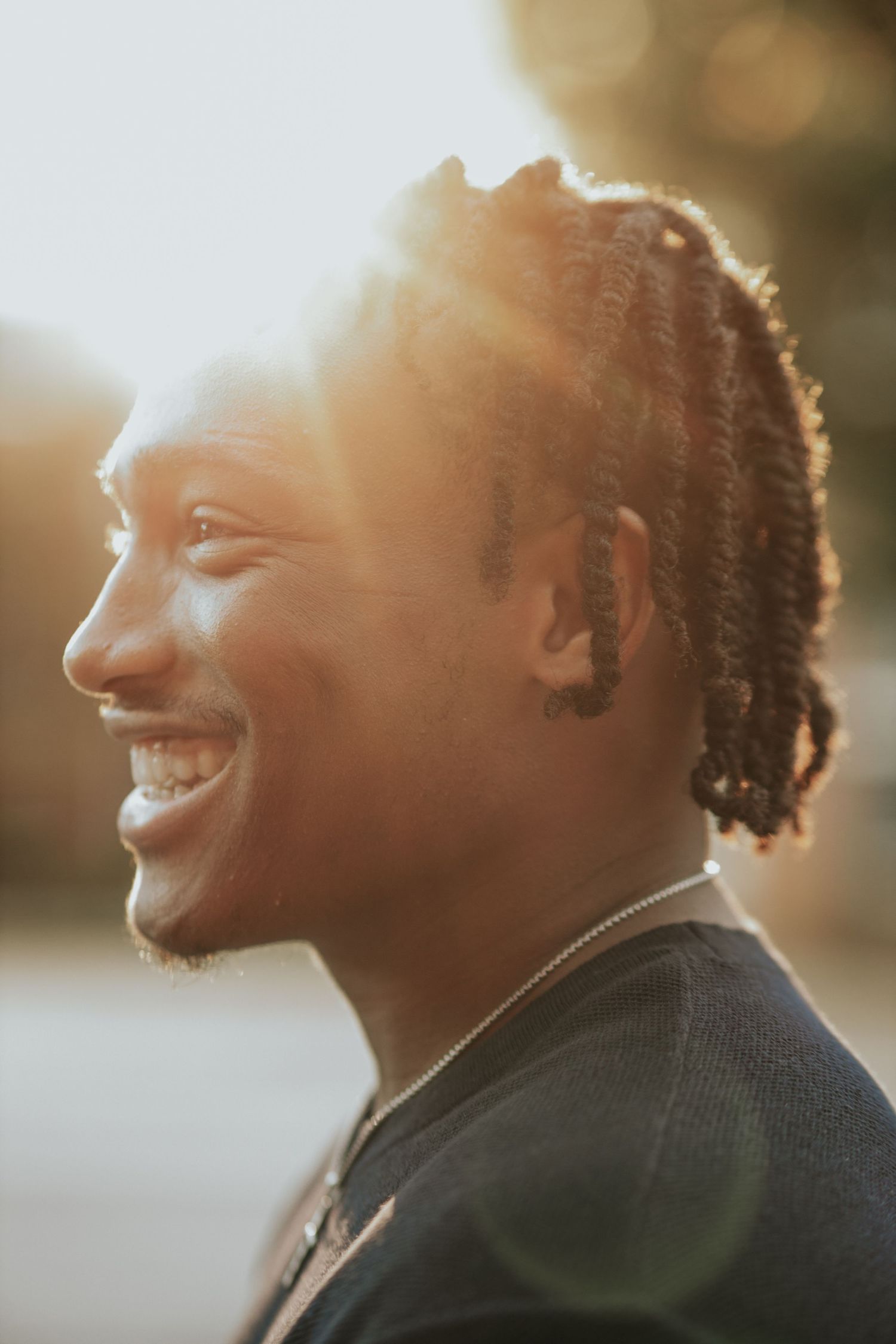 Profile portrait of a smiling person with braided hair backlit by golden sunlight.