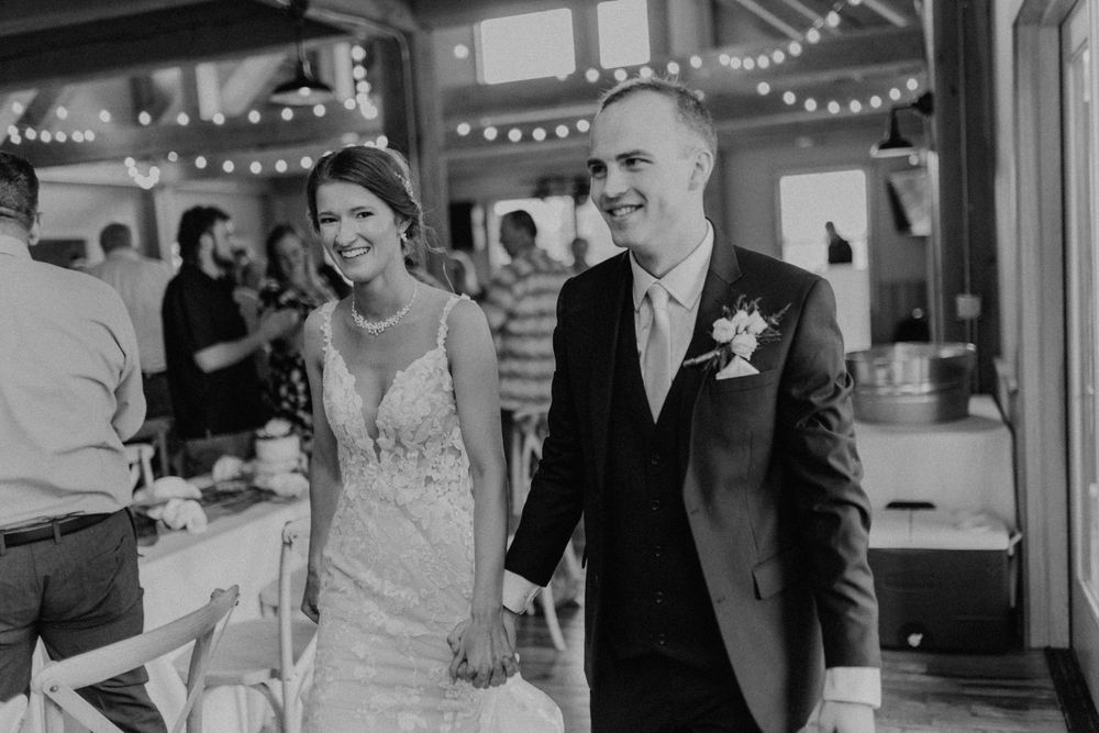 Black and white photo of joyful bride and groom walking into their rustic barn wedding reception.