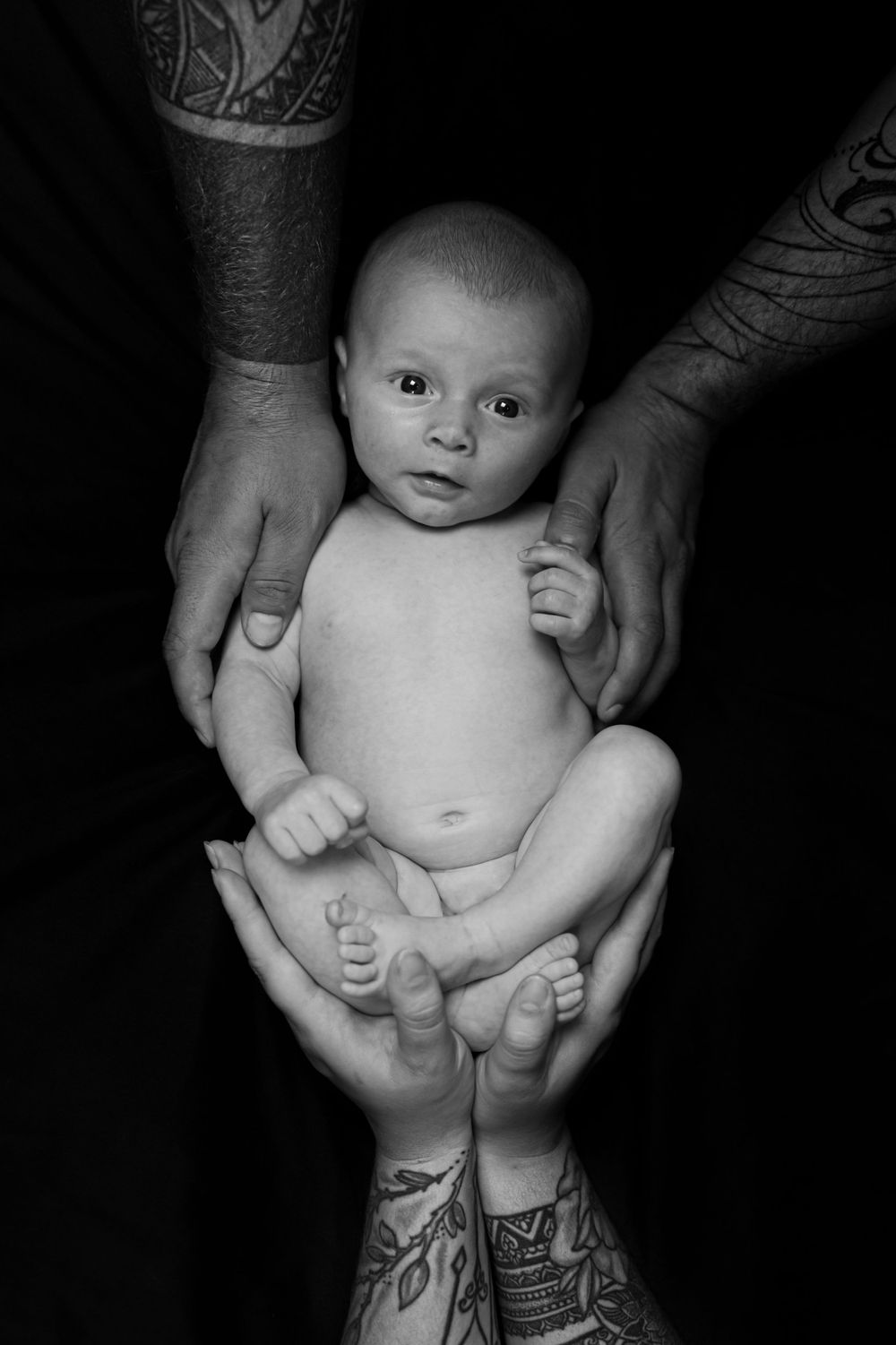 Black and white close-up of gentle hands cradling a newborn baby.