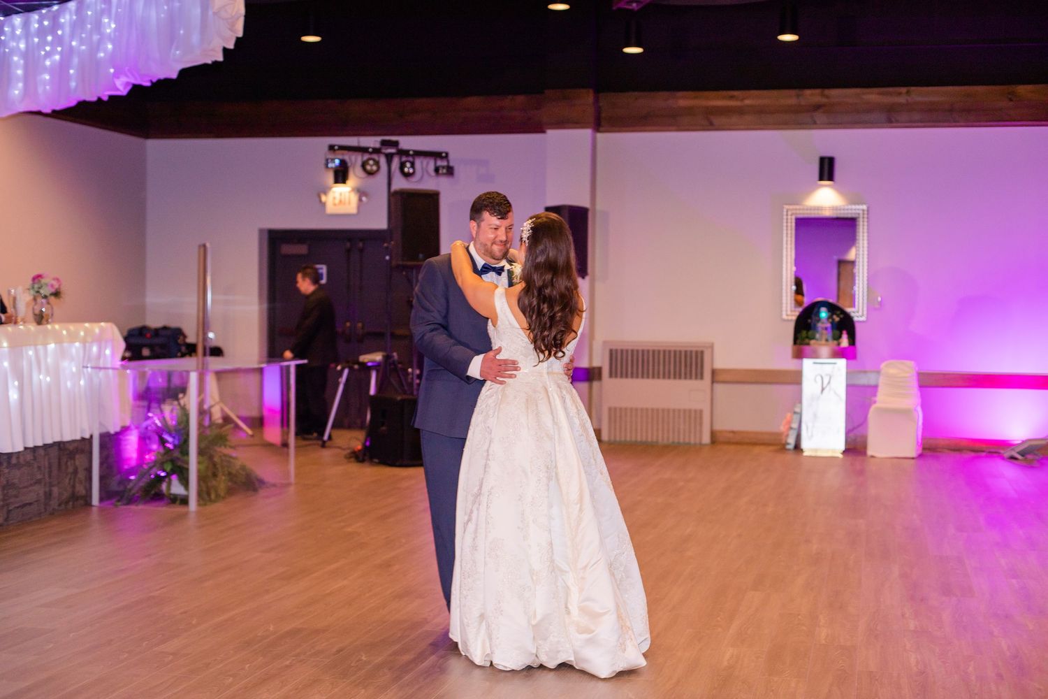 A couple shares their first dance at a wedding reception with purple lighting and white decor.
