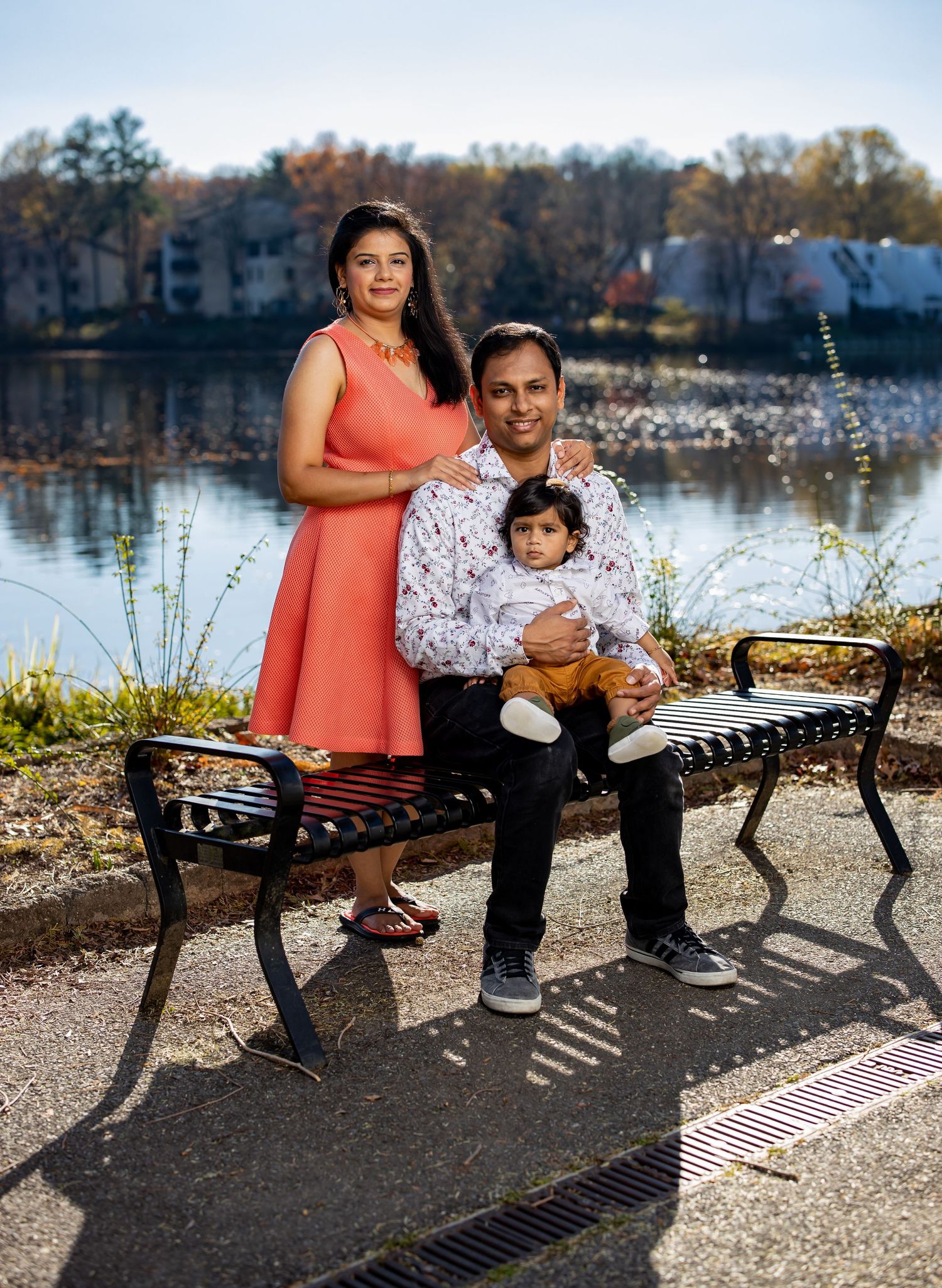 Family poses on bench by lakeside during autumn photo session.