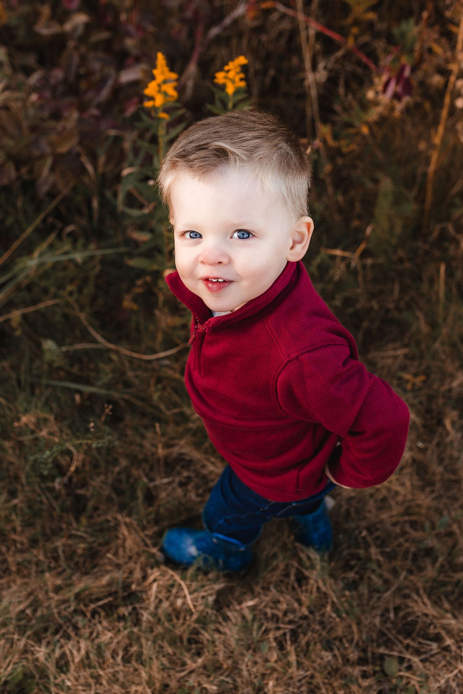 Young boy in red sweater looking towards camera, standing in a field