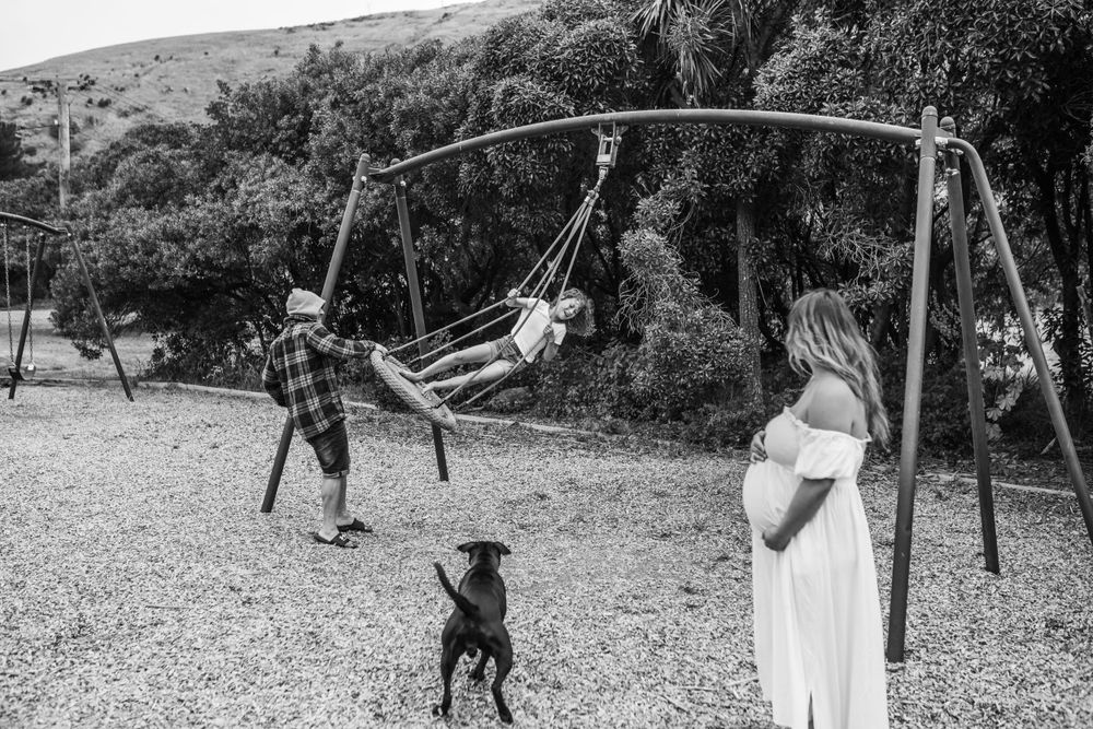 Black and white image of family and dog playing at a playground with swings.
