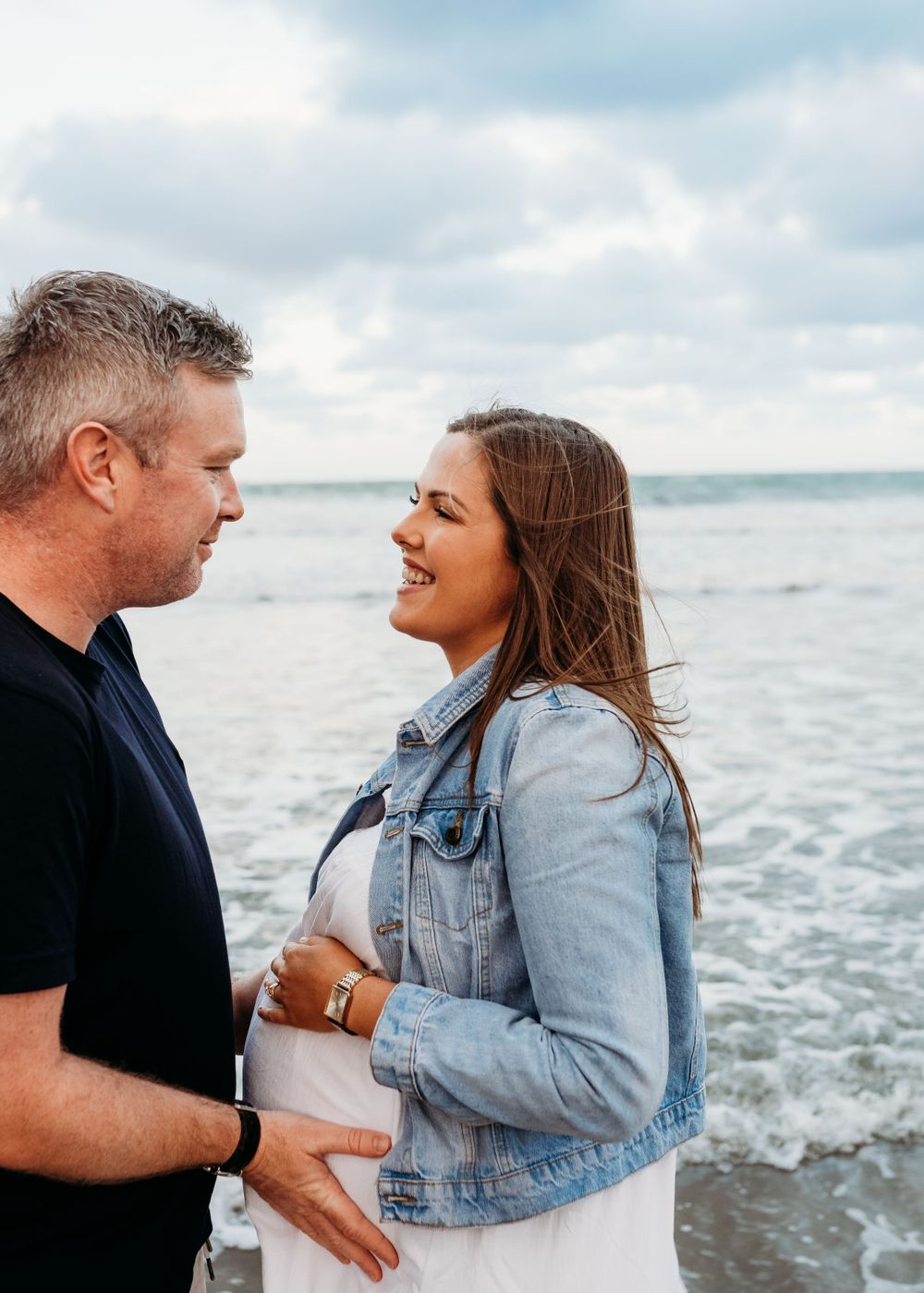 An expecting couple shares an intimate moment on the beach at sunset.