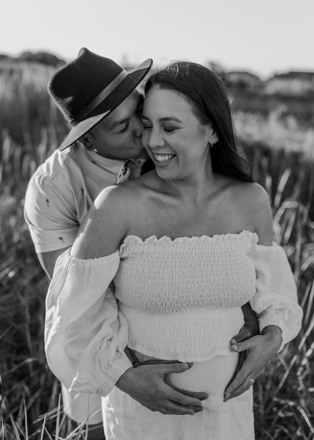A romantic maternity photo of a couple in a field at sunset.