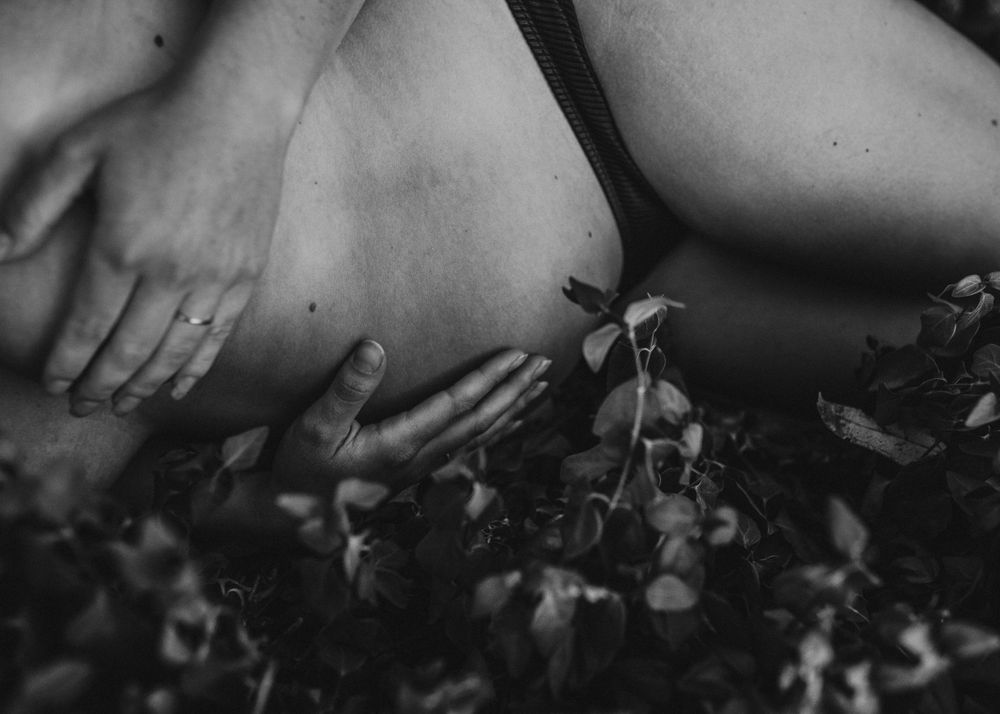Artistic black and white close-up of hands against foliage in natural light.
