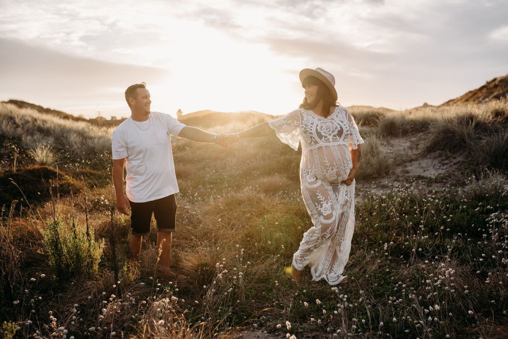 Couple playfully interacts in field of wildflowers during golden hour sunset.