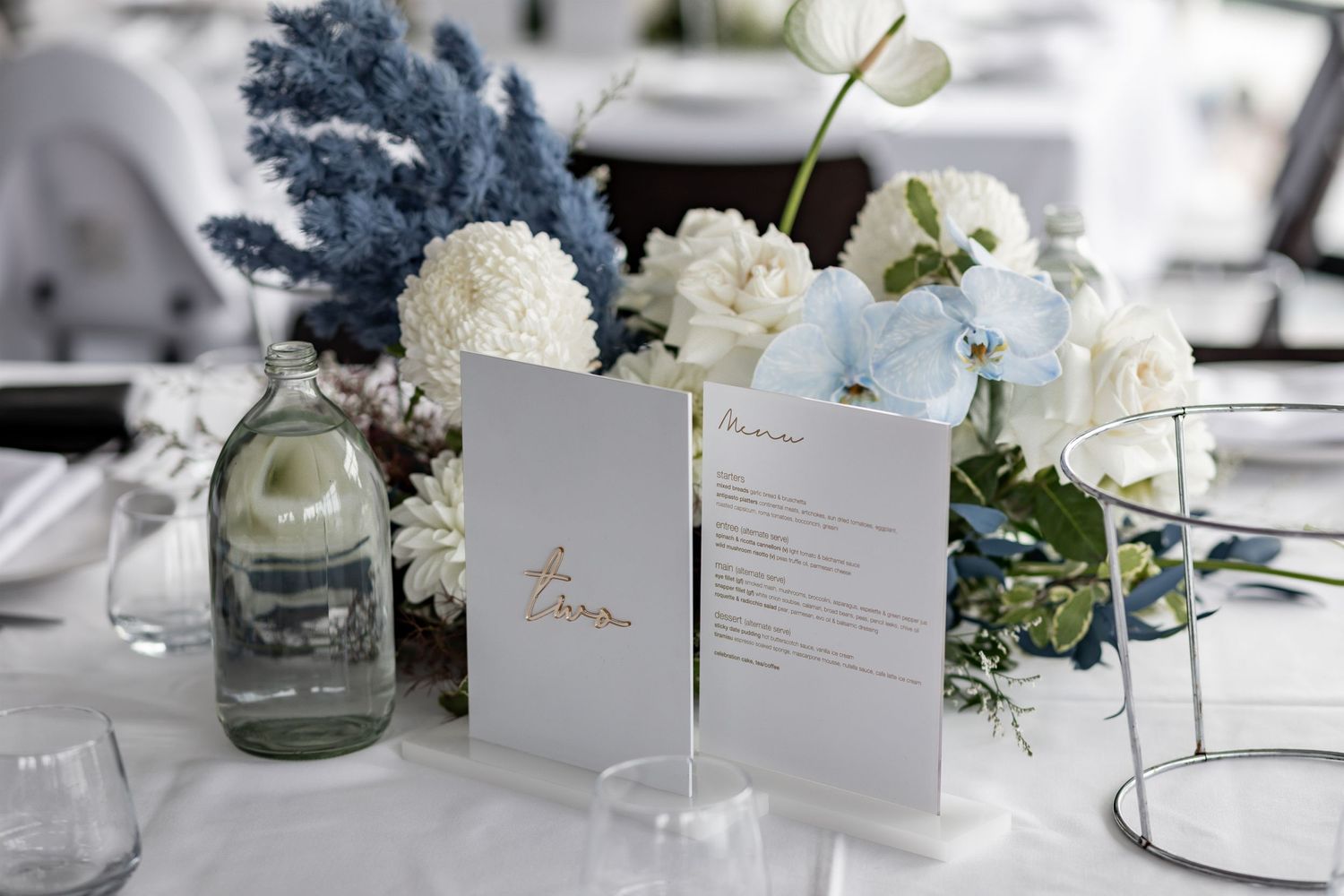 Wedding reception table setting with blue and white floral centerpiece and printed menu cards.