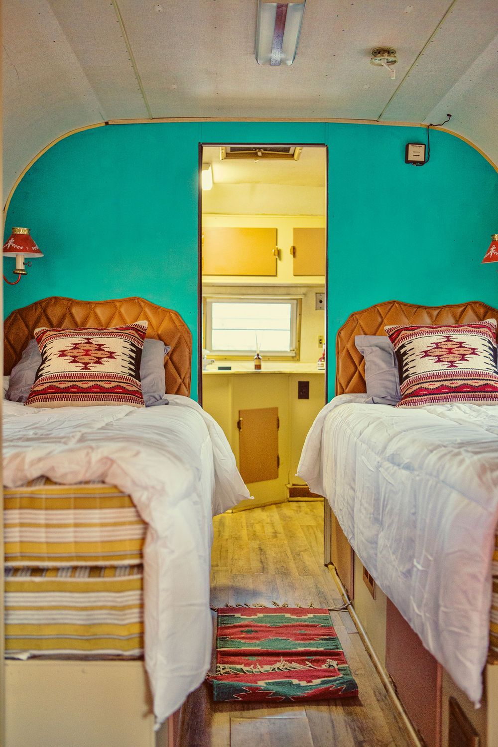Twin beds in a vintage trailer bedroom with teal arched wall, leather headboards, and southwestern-patterned pillows.