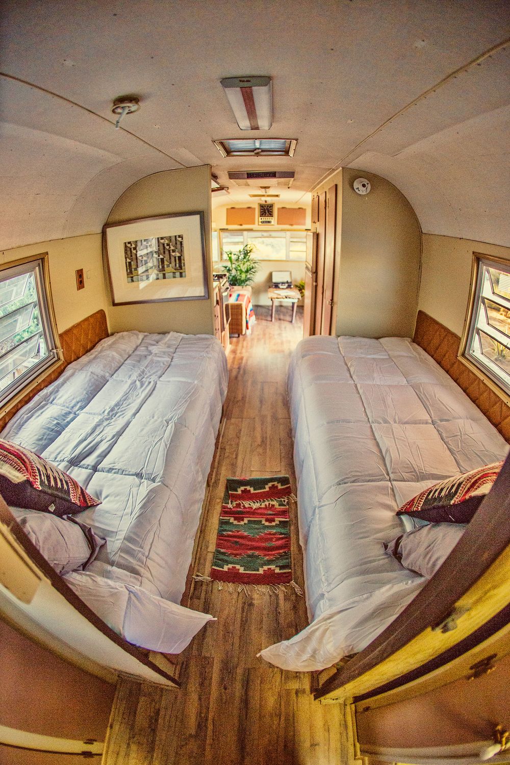 Interior of a vintage Airstream trailer converted into cozy sleeping quarters with two twin beds and hardwood floors.
