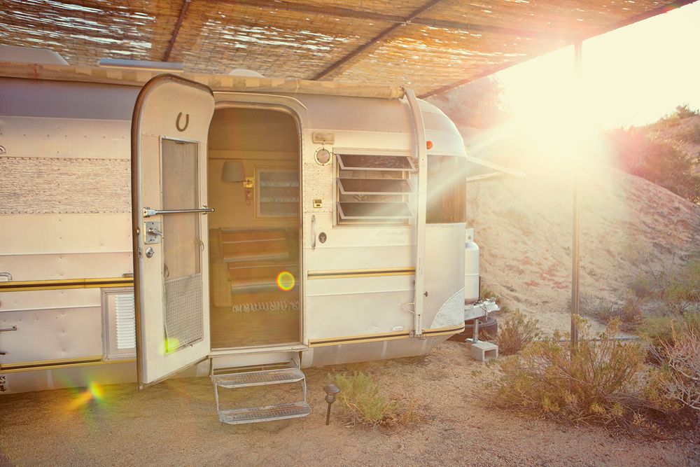 Vintage cream travel trailer with open door and horseshoe detail, bathed in warm golden desert sunlight.