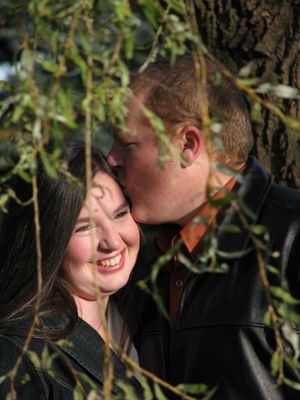 A couple intimately kissing and smiling behind a willow tree