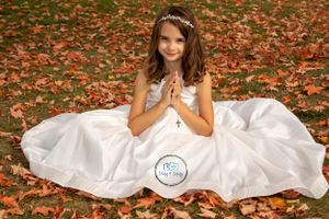 A young girl in a communion dress sitting amongst the fallen fall leaves