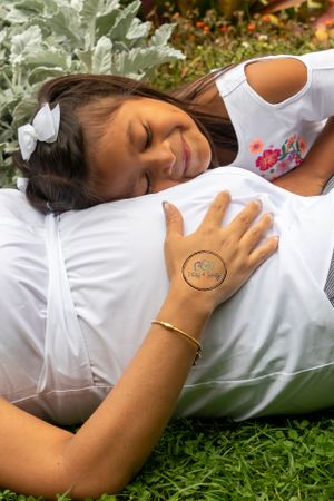 A young child hugging her mom's pregnant belly lying down