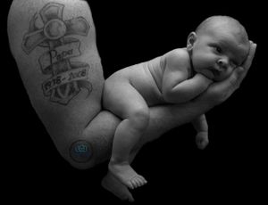 A black and white photo of a tatooed arm holding a newborn baby