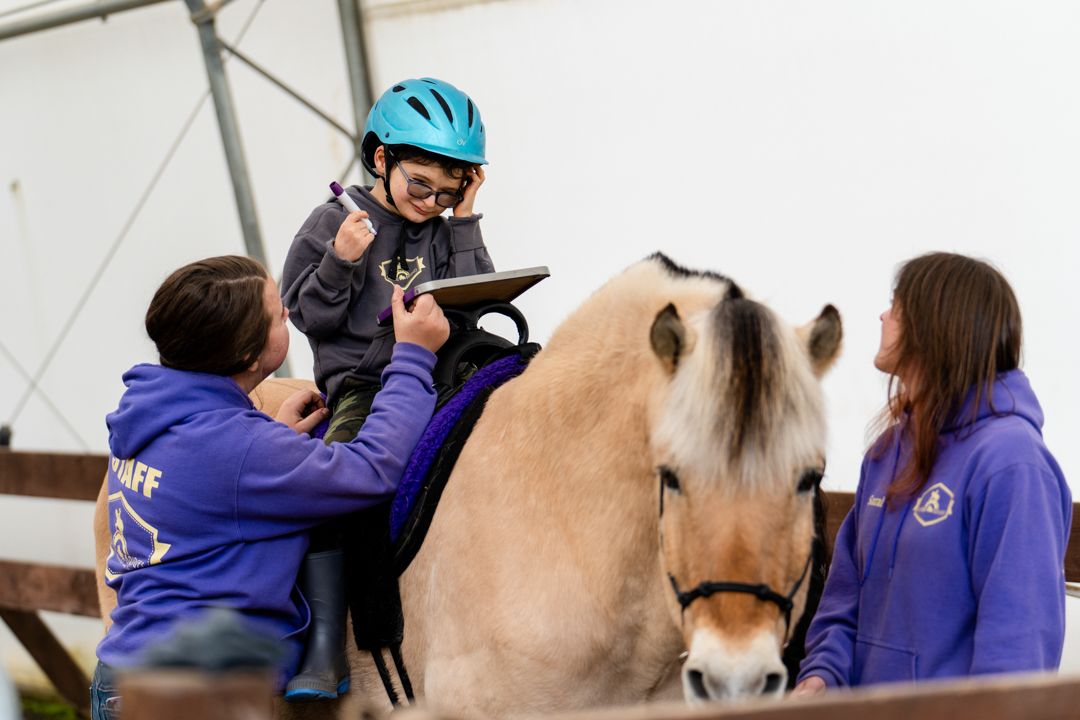 boy works on drawing on a white board while sitting on a horse