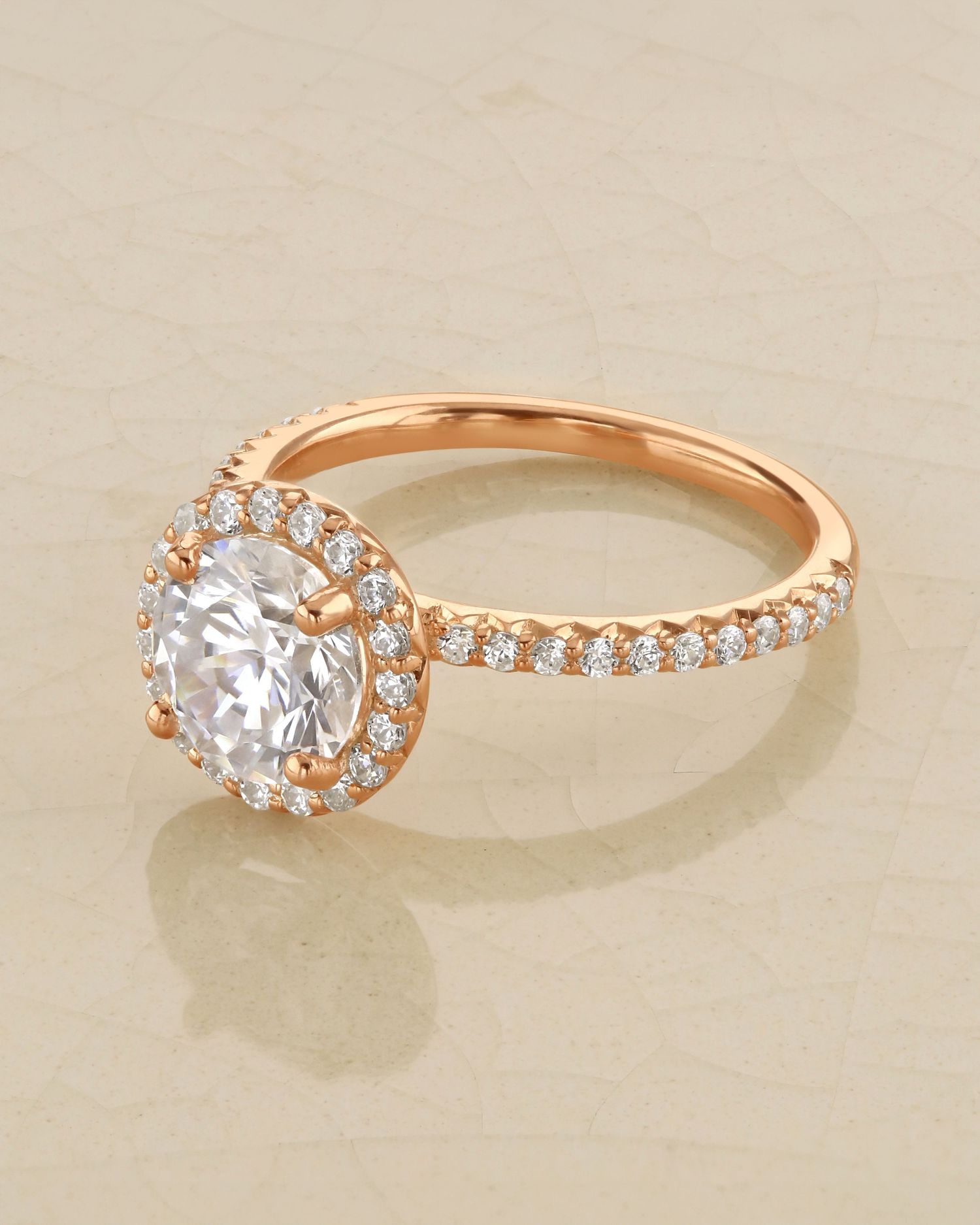 Rose gold engagement ring with round center stone surrounded by diamond halo and pave band.