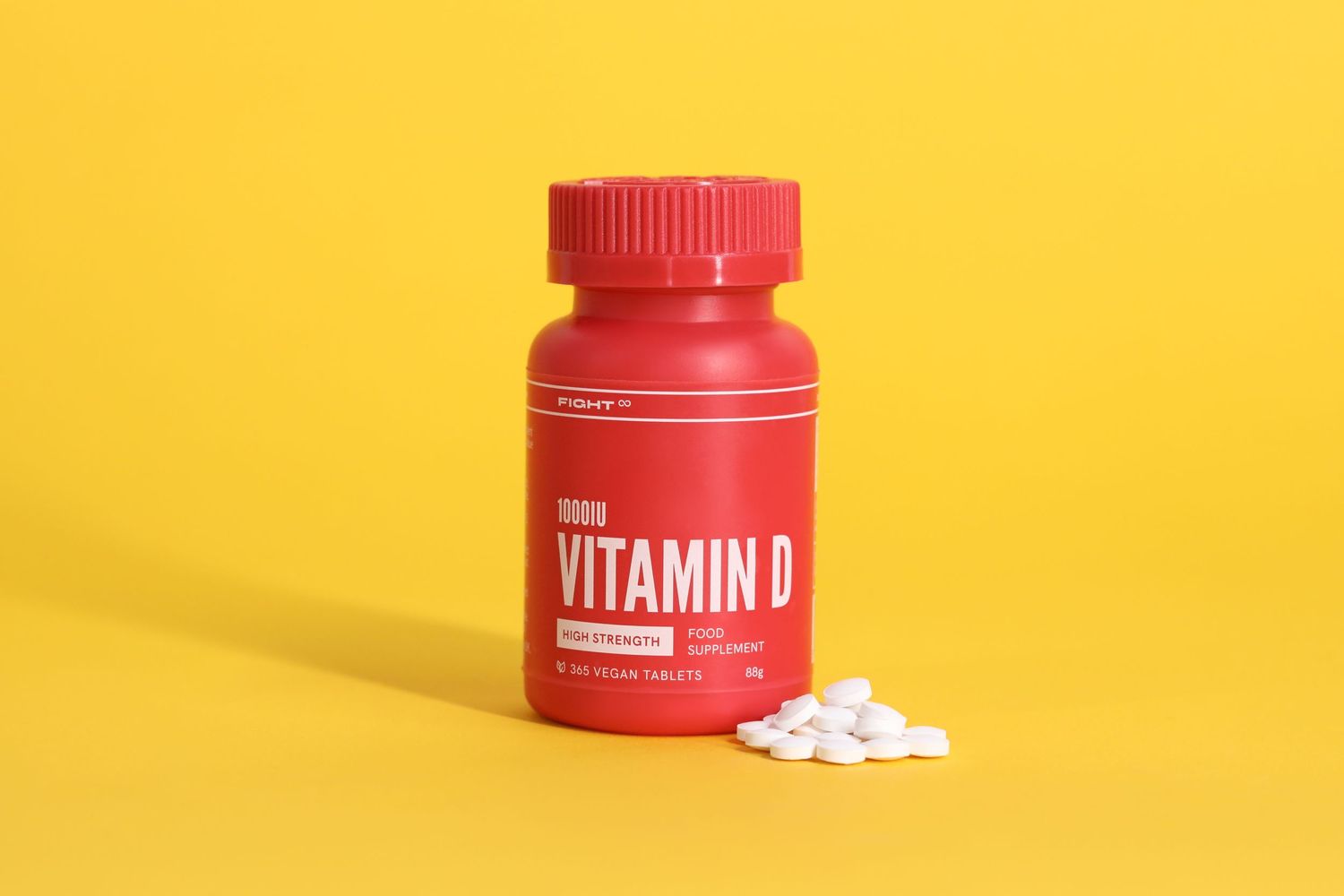 Red vitamin D supplement bottle with white tablets spilled on yellow surface.