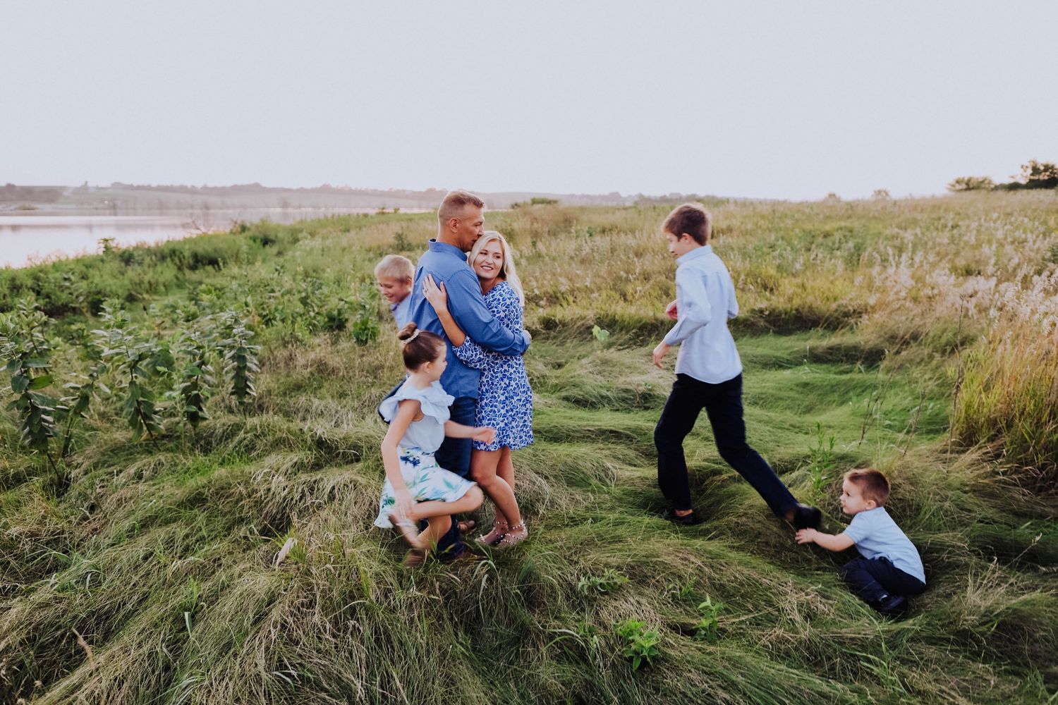 Family members playing and running through tall grass in an open field.