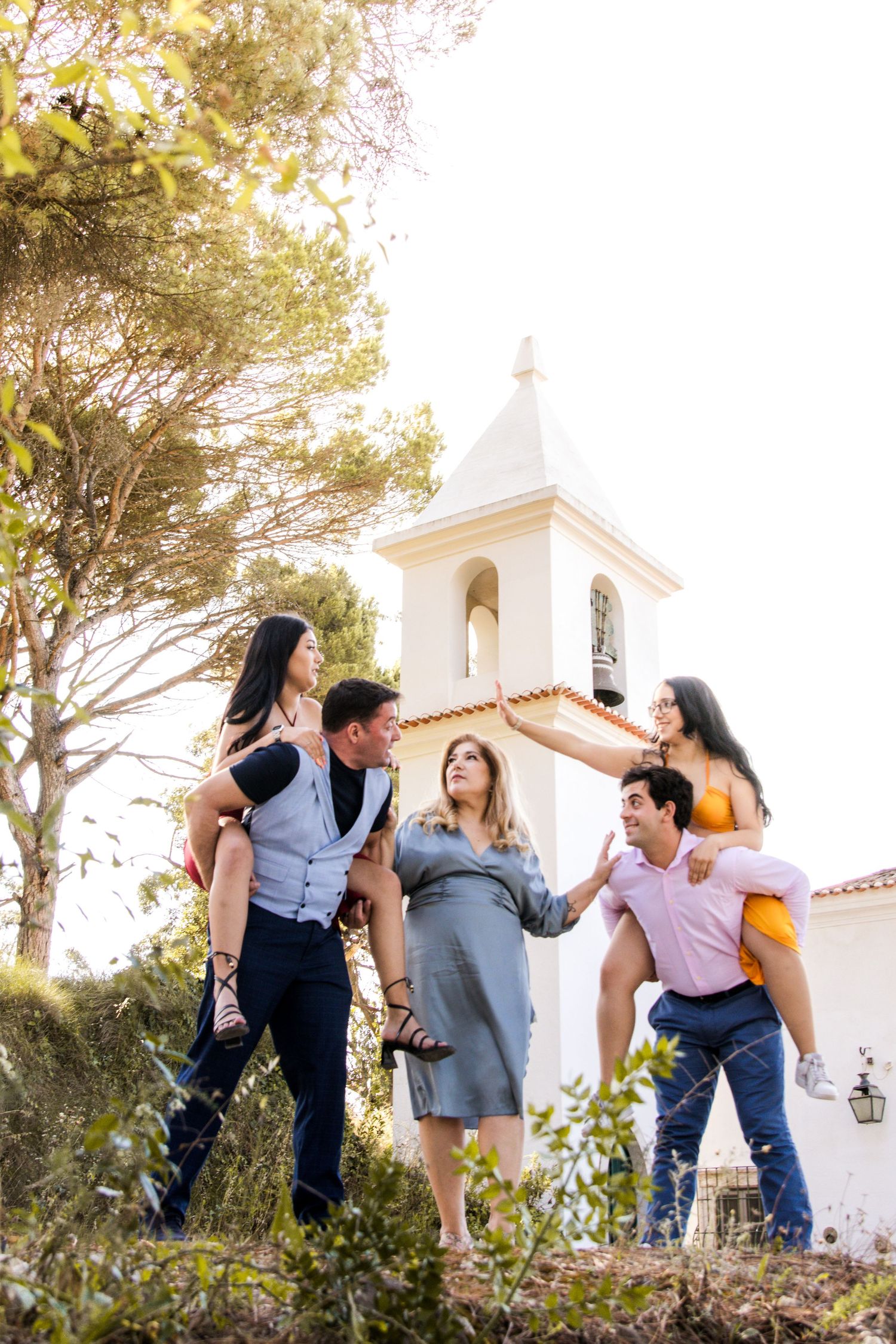 Family members playfully pose together outdoors near a white church building in casual attire.